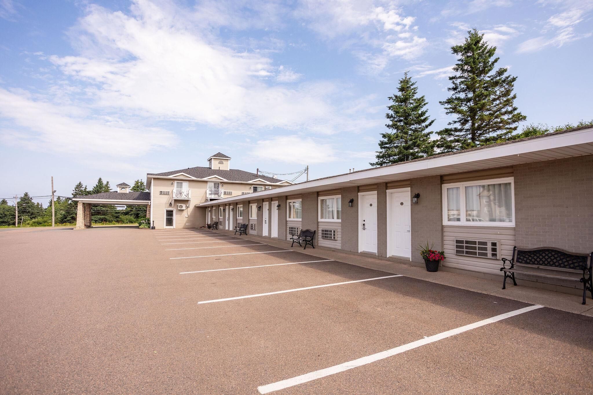 Un motel con un parcheggio, camere individuali con finestre e un edificio sullo sfondo.