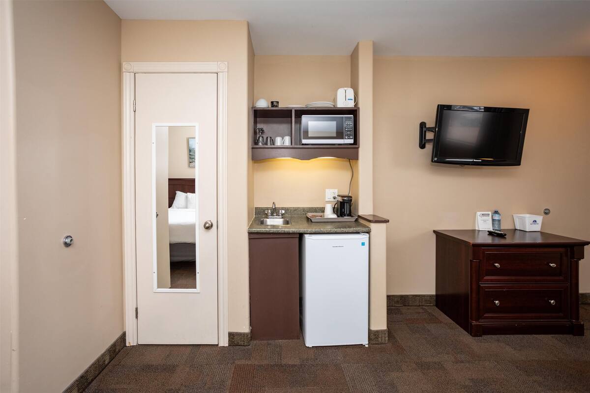 A compact kitchenette with a microwave, coffee maker, and small refrigerator. A flat-screen TV is mounted on the wall above the counter.