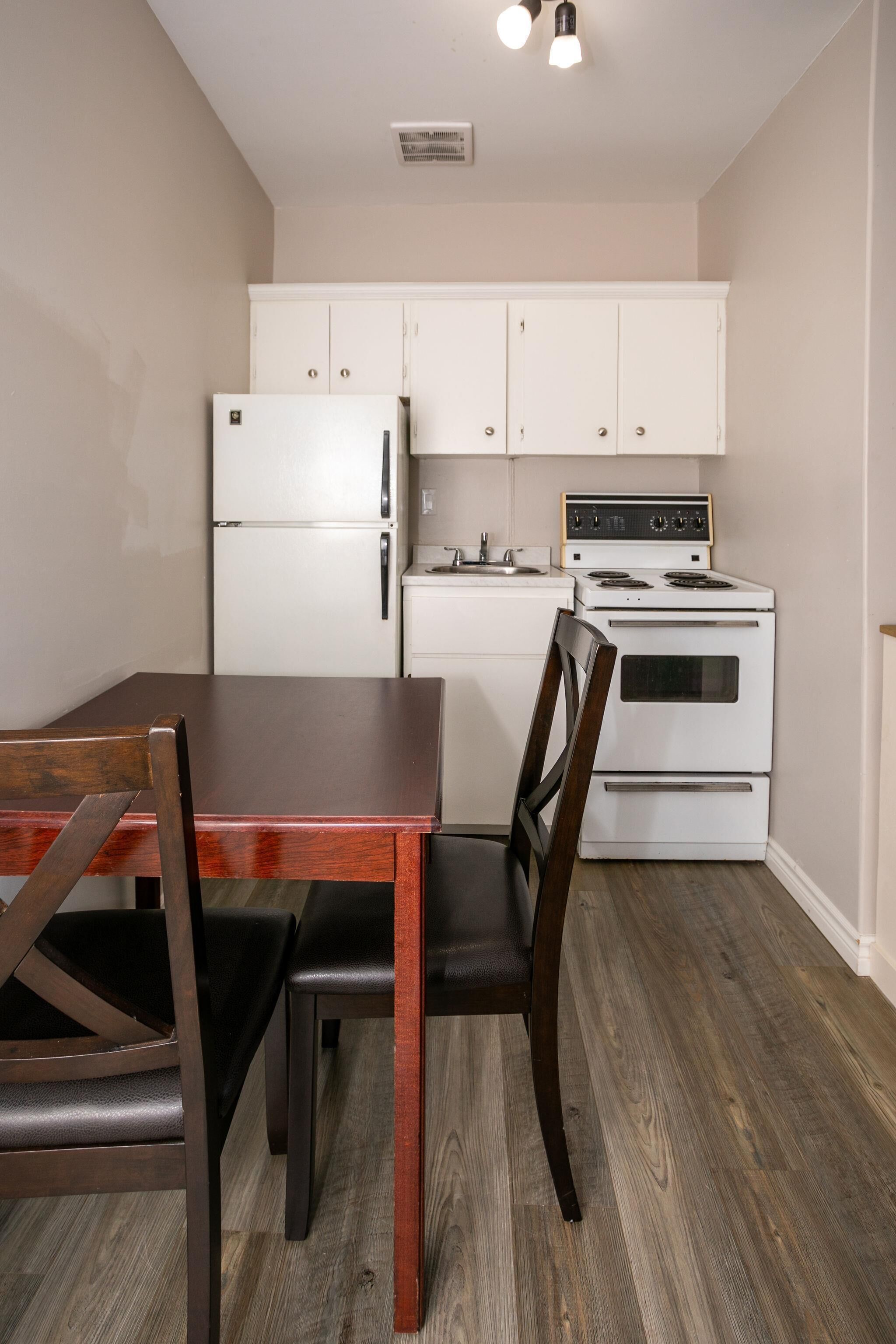 Une cuisine compacte avec des meubles blancs, un réfrigérateur, une cuisinière et une table à manger avec des chaises.
