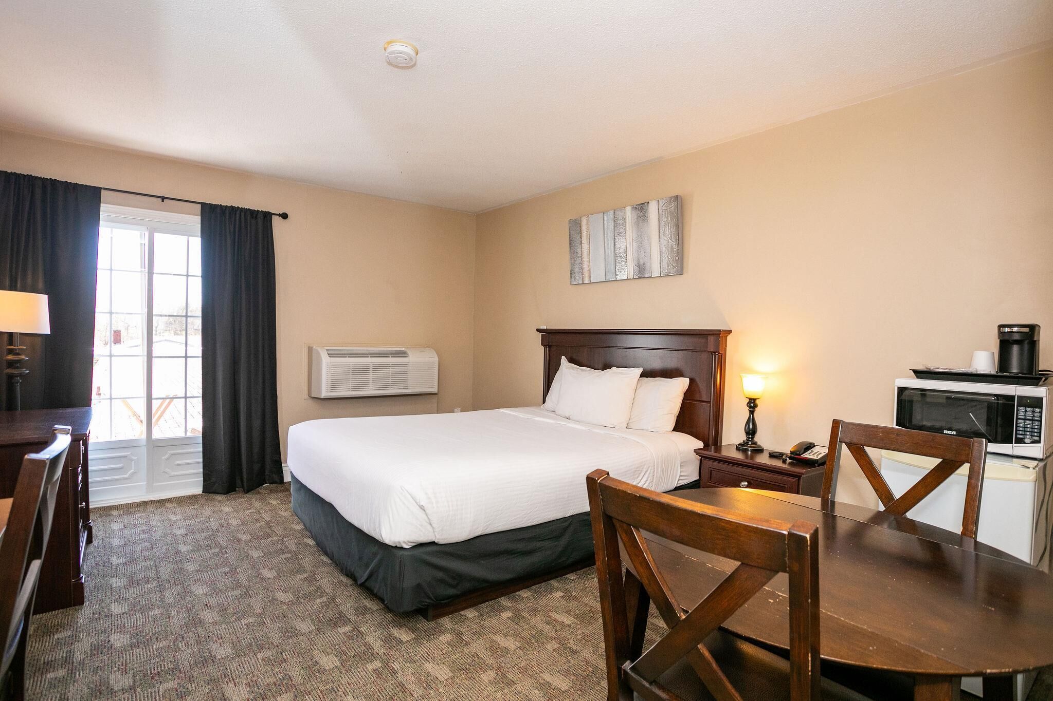 A hotel room with a bed, a desk, a chair, a microwave, and a coffee maker.