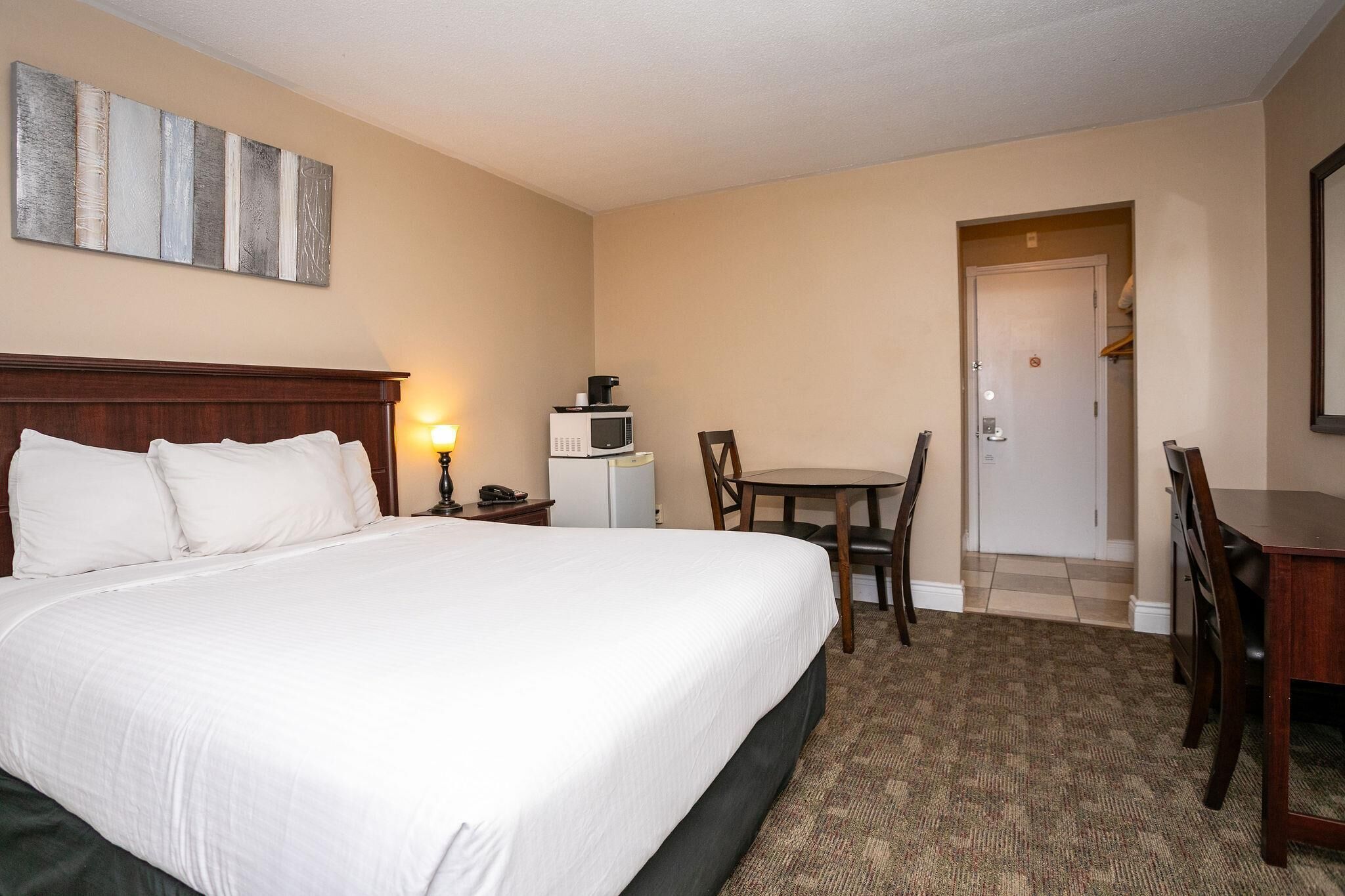 A hotel room with a large bed, a dining table, a microwave, and a door leading to a closet.