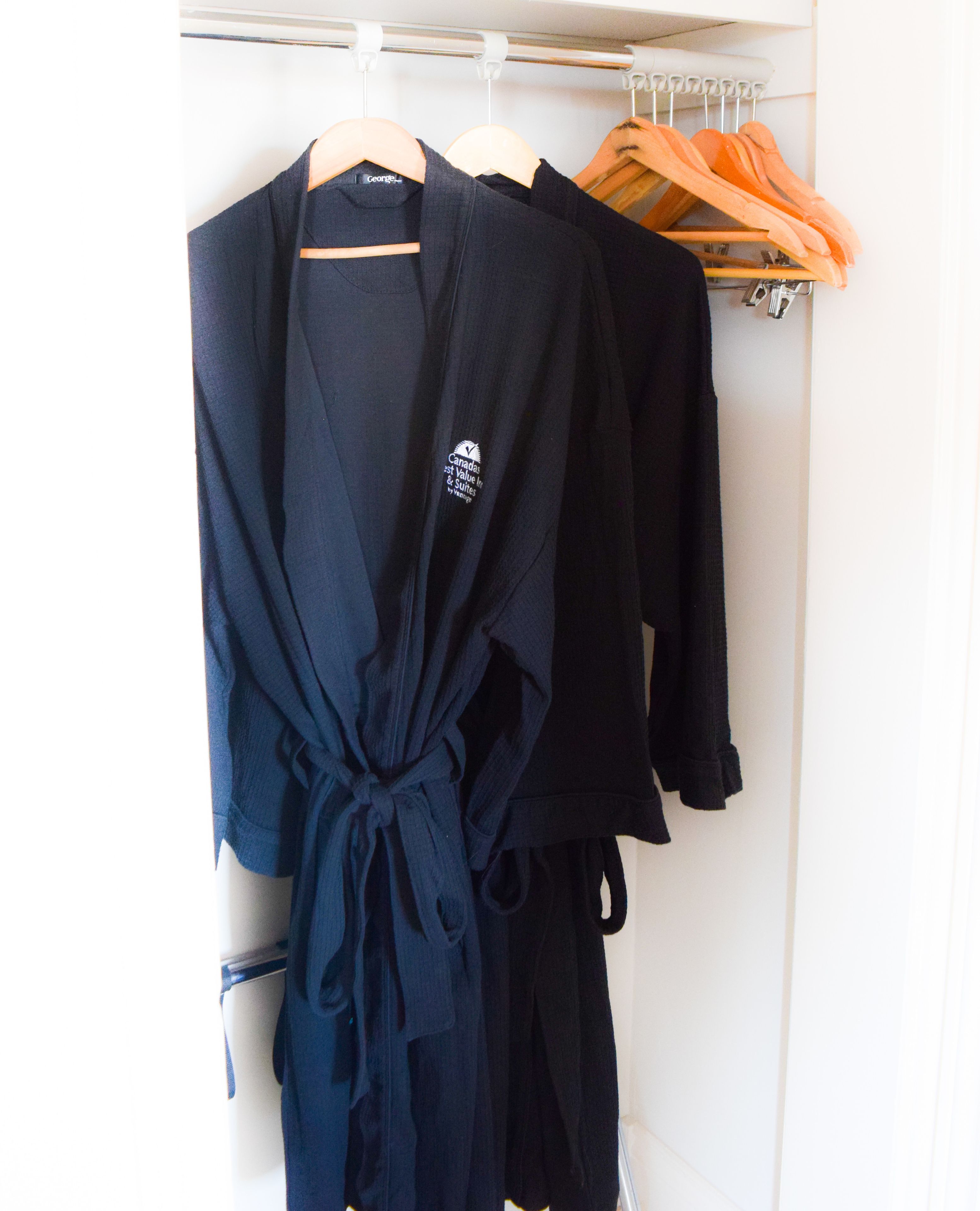 A closet with various clothing items, including a dark blue robe with a logo and a black cardigan.