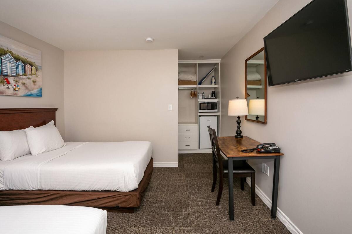 A hotel room with a bed, a desk with a lamp, a television, and a closet with a microwave.
