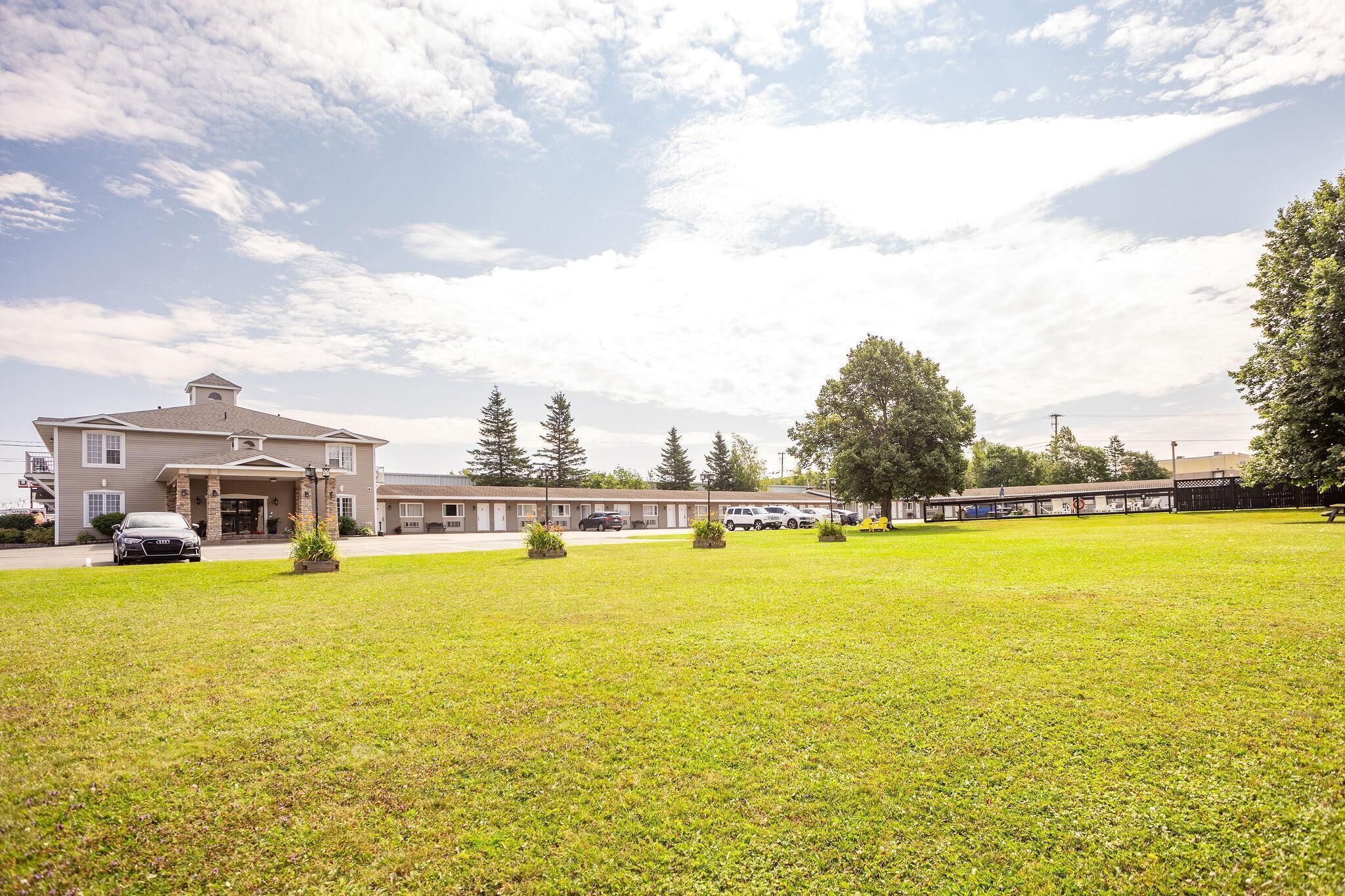 A hotel with a large lawn, multiple parking spaces, and a building with a prominent entrance.