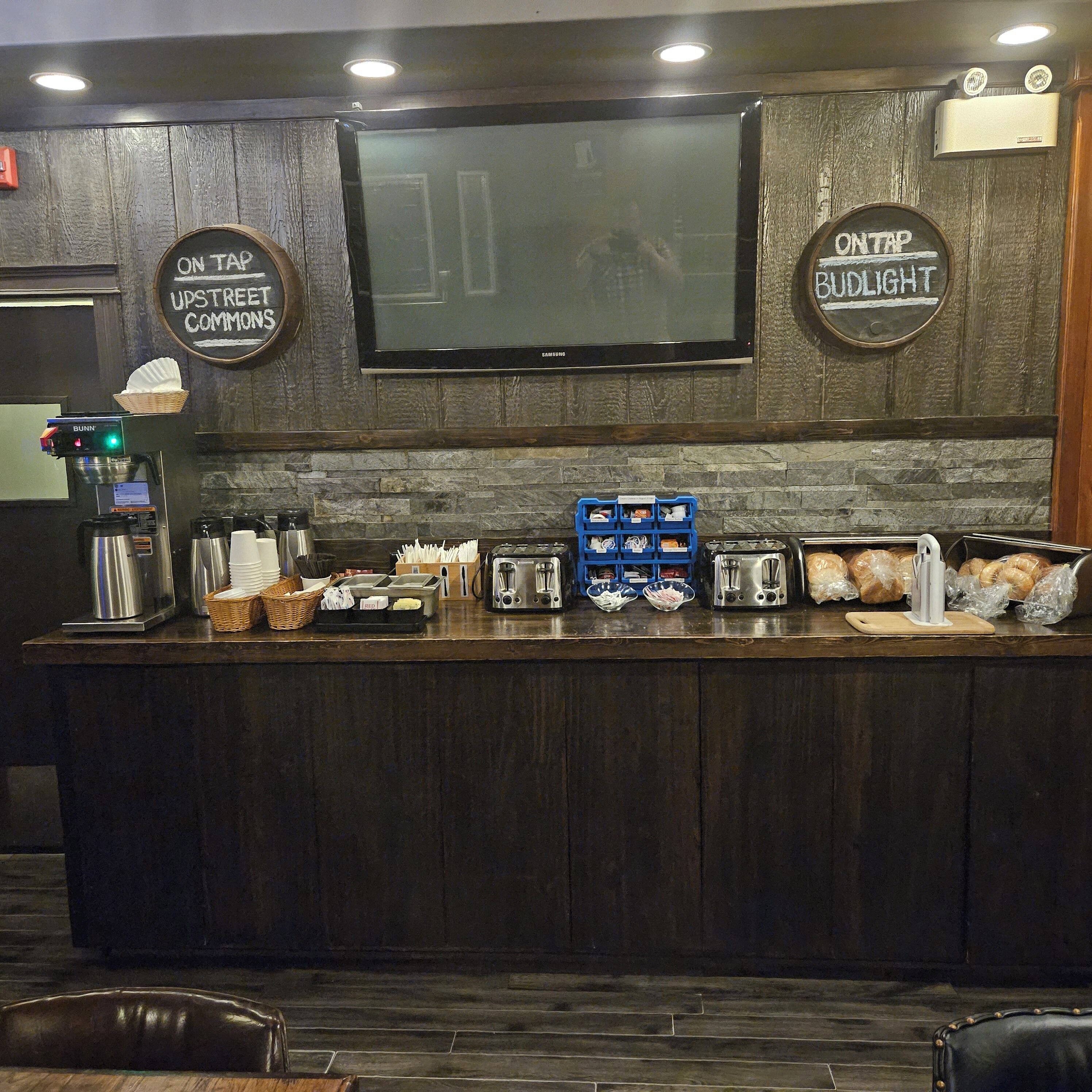 A bar area with a television, a coffee machine, and various food items.