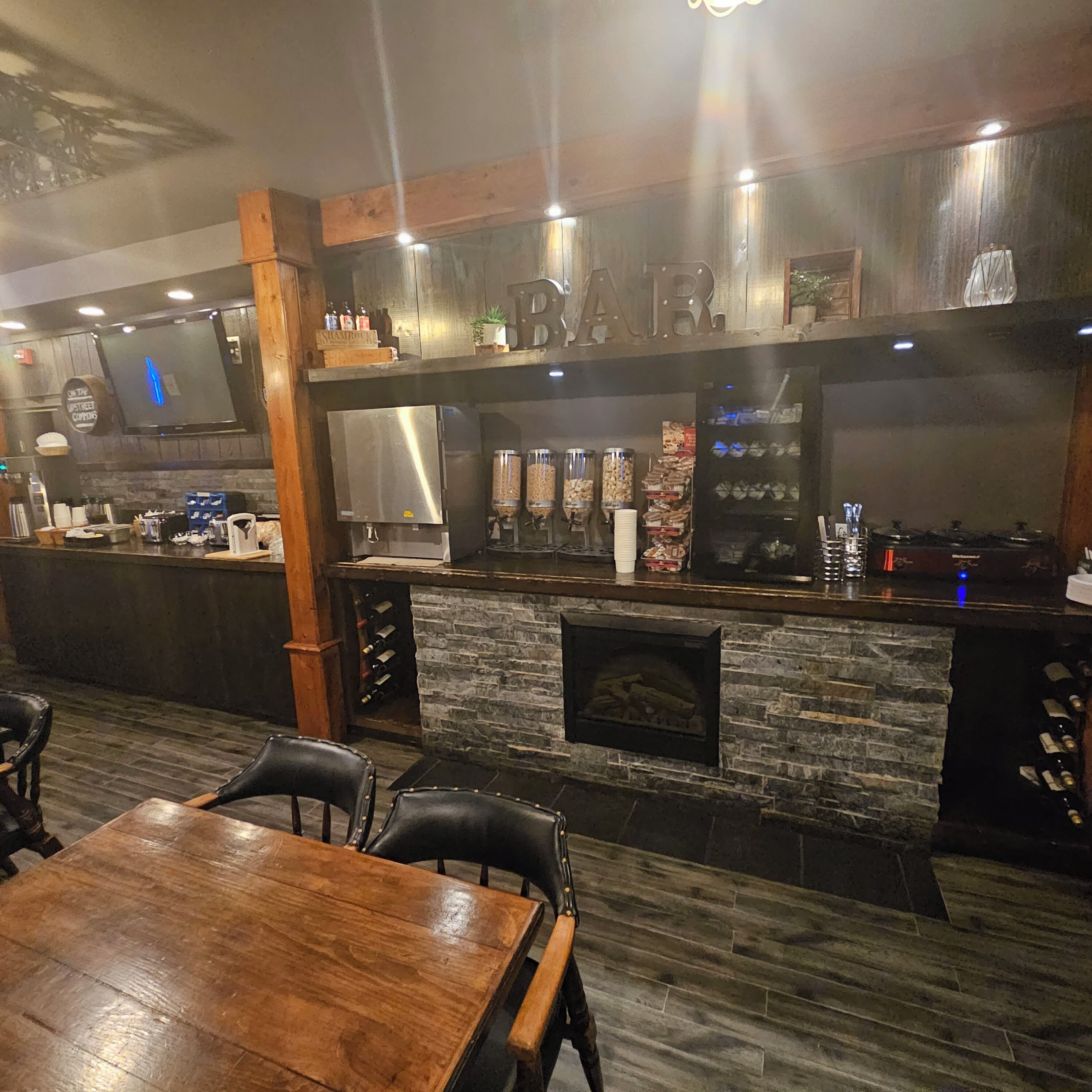 Un área de bar con chimenea de piedra, barra de madera y asientos.