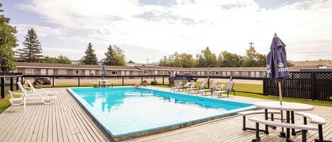 Una piscina rectangular con muelle de madera, sillas de descanso y una mesa de picnic.
