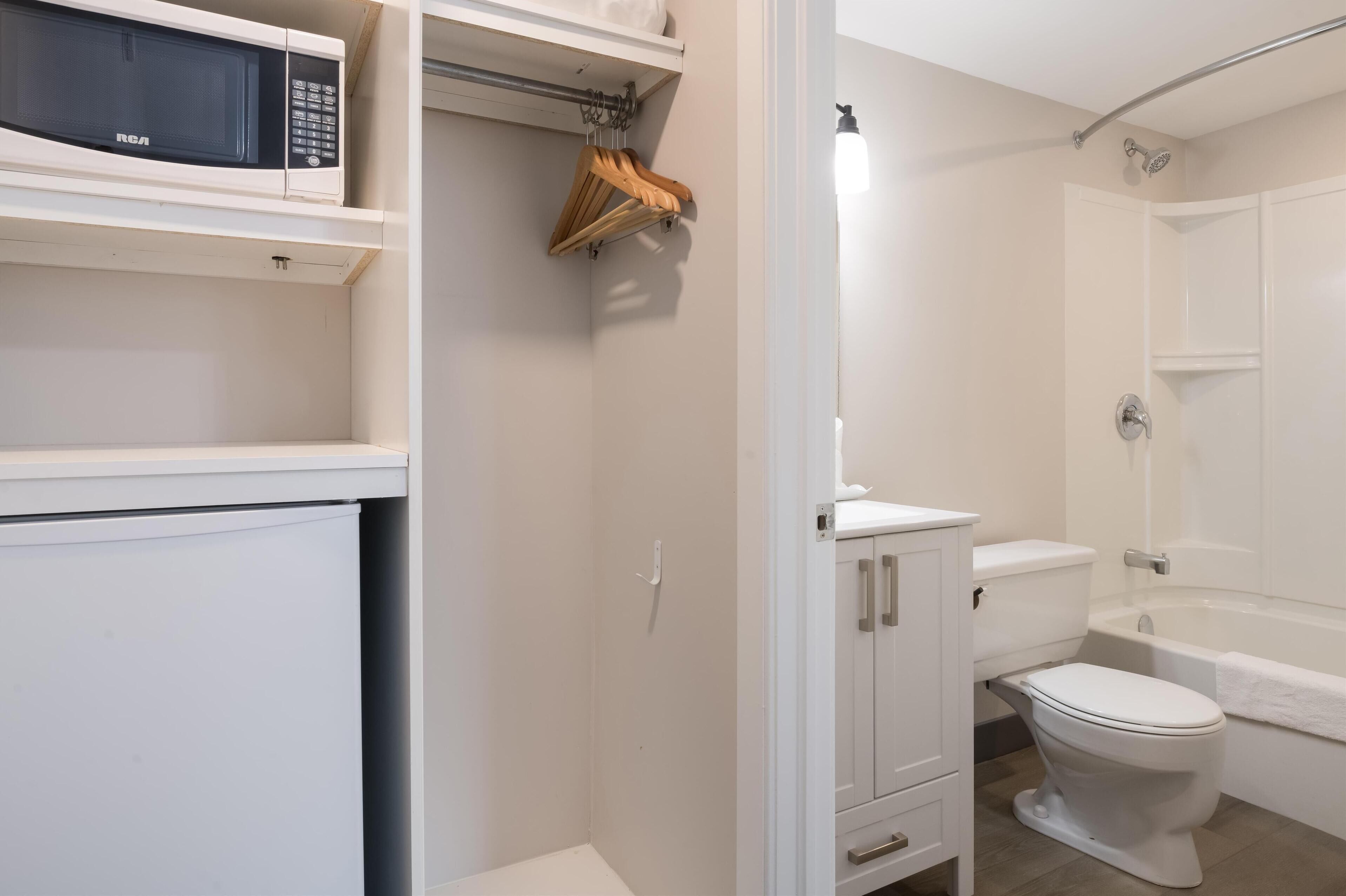 A bathroom with a toilet, bathtub, and a microwave on a shelf.
