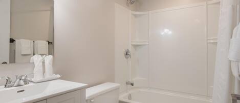 Un bagno moderno con lavandino, water e vasca da bagno bianchi. Asciugamani appesi al muro e tenda da doccia.