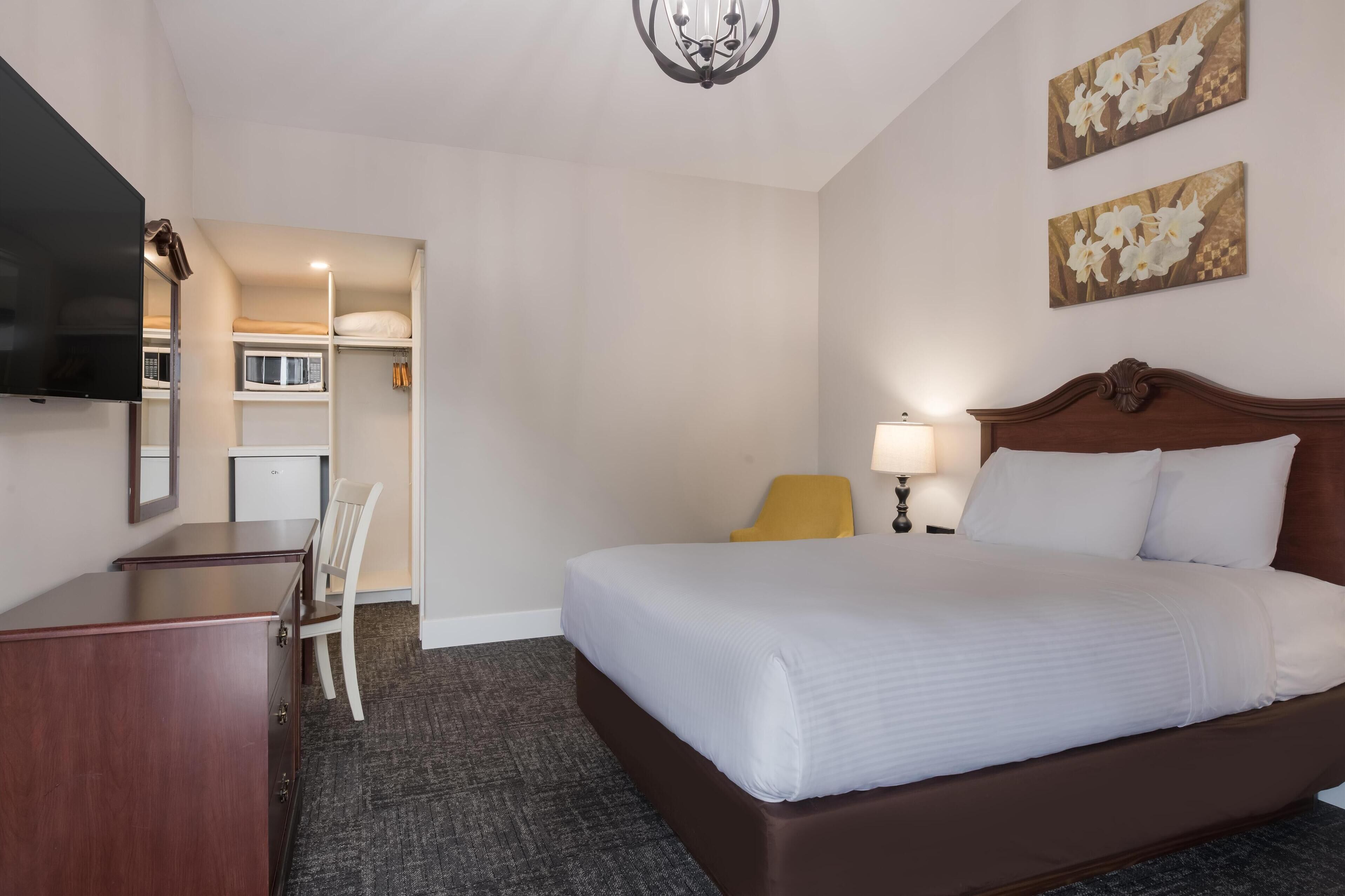 A hotel room with a bed, a desk, a chair, a TV, a lamp, and artwork on the walls.