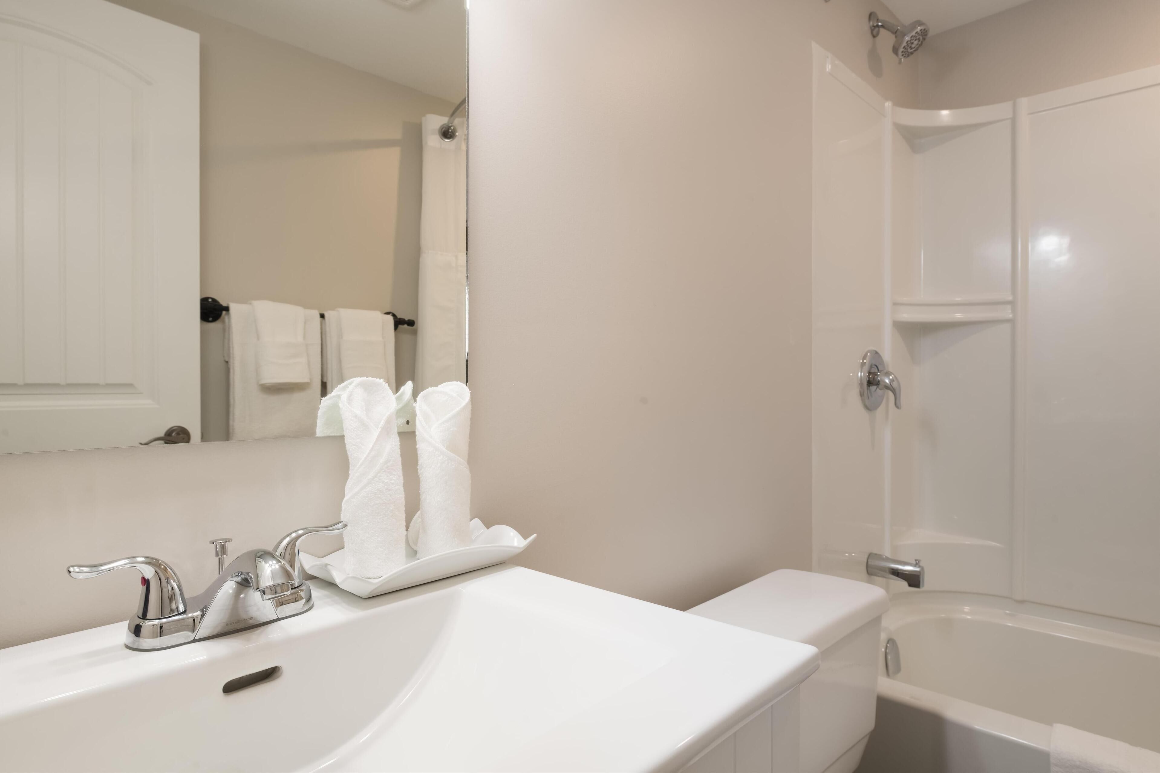 Un baño con un lavamanos blanco, un espejo, un perchero con toallas blancas y una bañera.