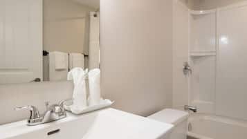 A bathroom with a white sink, a mirror, a towel rack with white towels, and a bathtub.