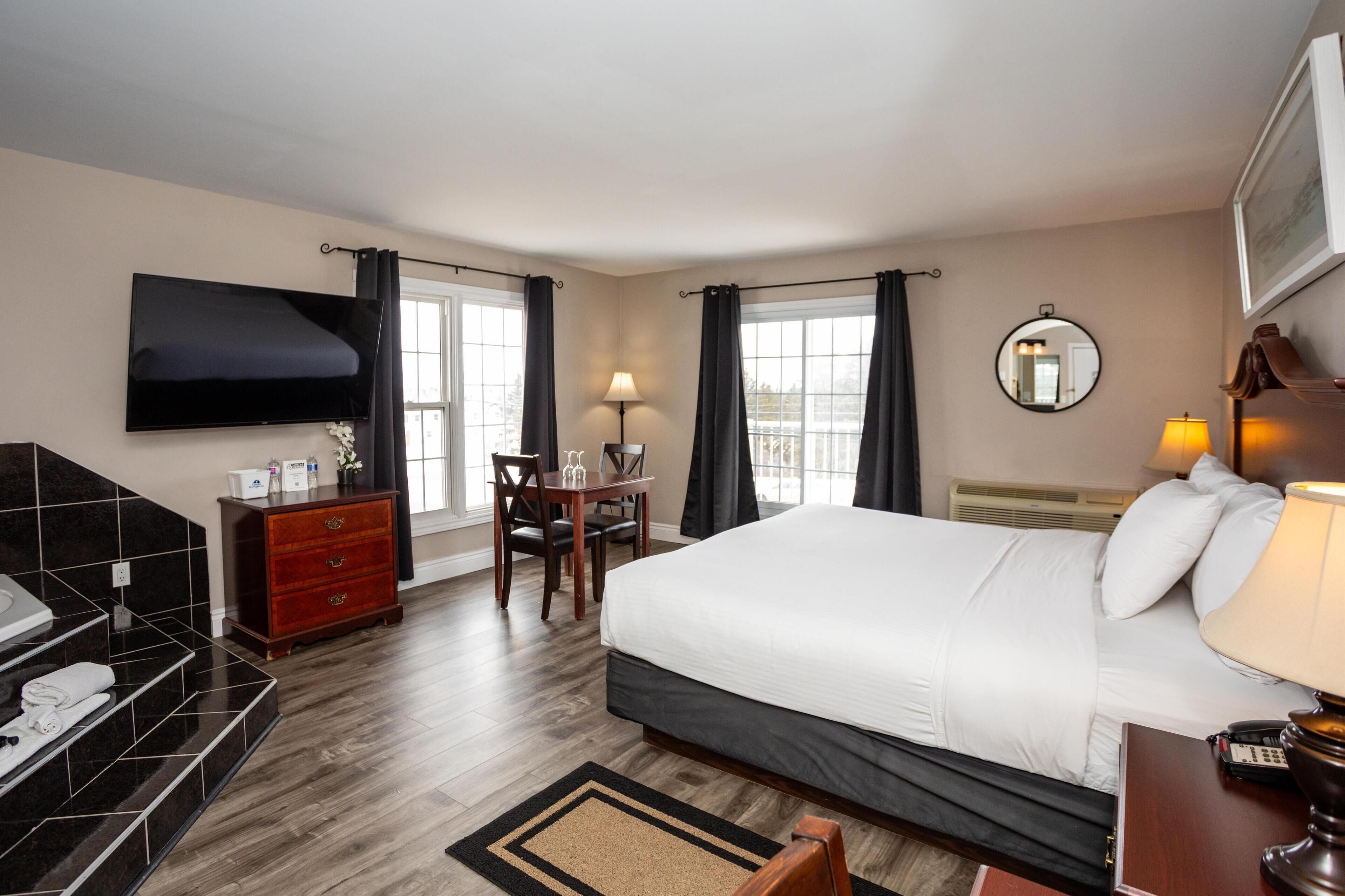 A hotel room with a large bed, a desk, a chair, a TV mounted on the wall, and a bathroom with a sink and mirror.