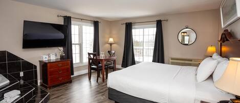 Una habitación de hotel con una cama grande, un escritorio, una silla, un televisor montado en la pared y un baño con lavamanos y espejo.