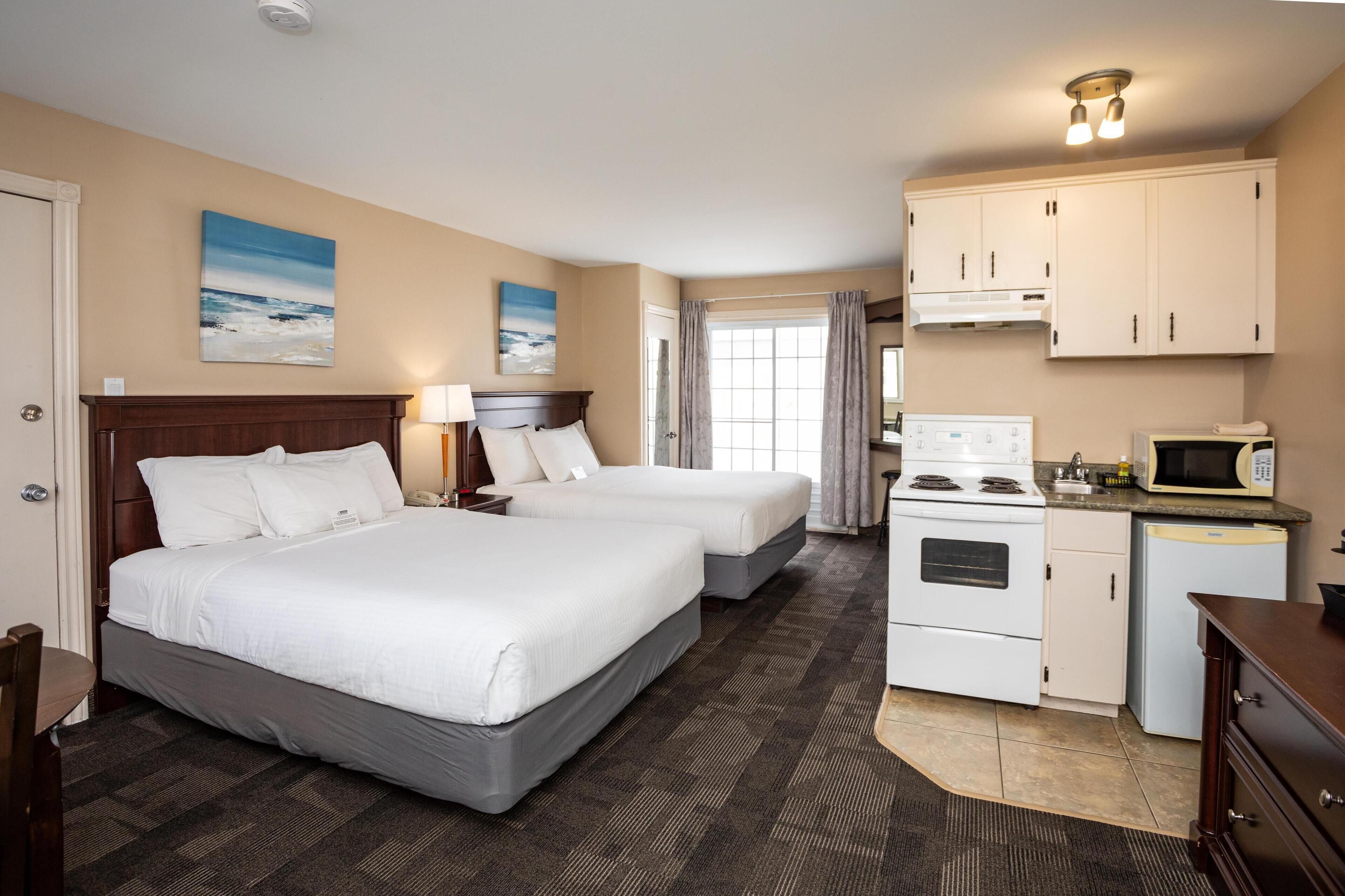 Een hotelkamer met twee bedden, een kitchenette, een magnetron en een fornuis.