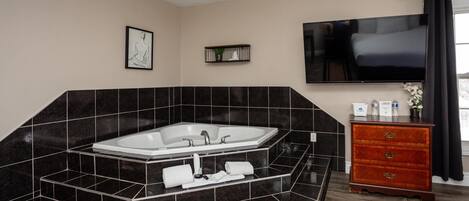 Un baño moderno con una bañera independiente, un tocador con cajones, un televisor de pantalla plana montado sobre la bañera y un cuadro enmarcado en la pared.