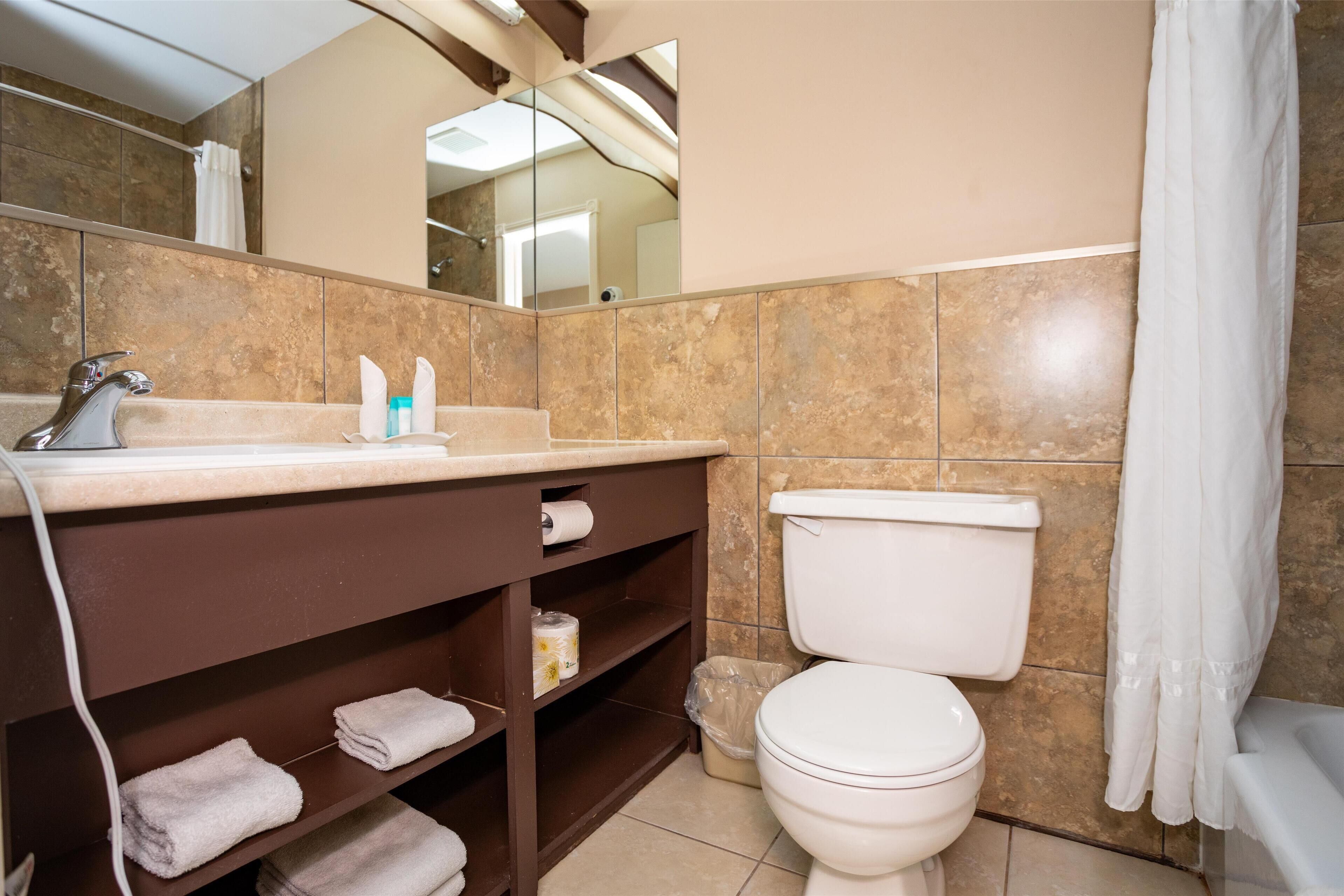 Une salle de bain équipée de toilettes, d’un lavabo et d’étagères où sont rangées les serviettes.