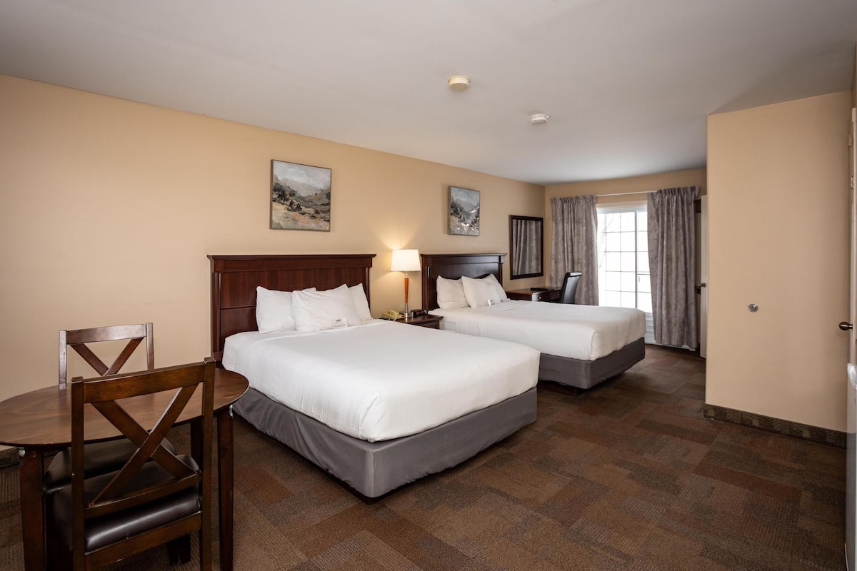 A hotel room with two beds, a wooden chair, a desk, and a window with curtains.