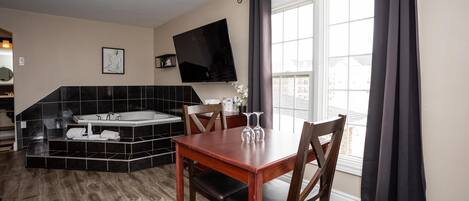 Una cocina moderna con estufa integrada, un comedor con mesa y sillas de madera, un ventanal con cortinas y un televisor de pantalla plana montado en la pared.