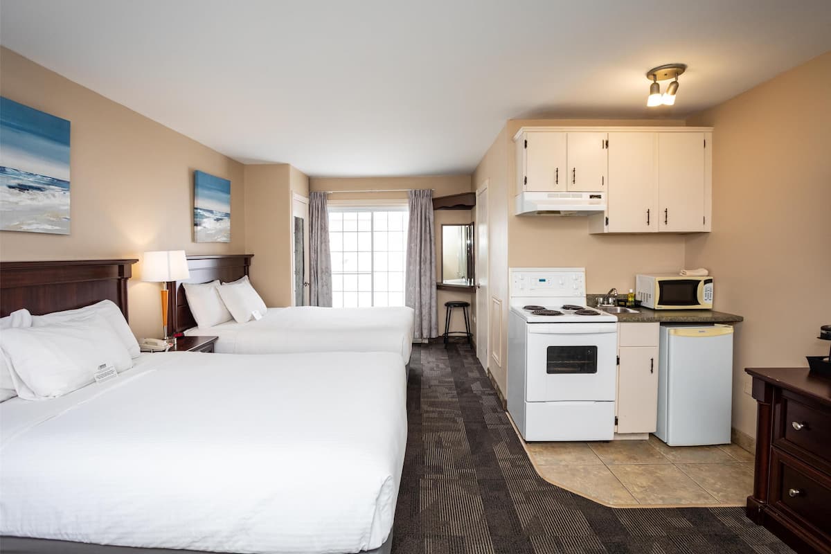 A hotel room with two beds, a kitchenette, a microwave, and a stove.
