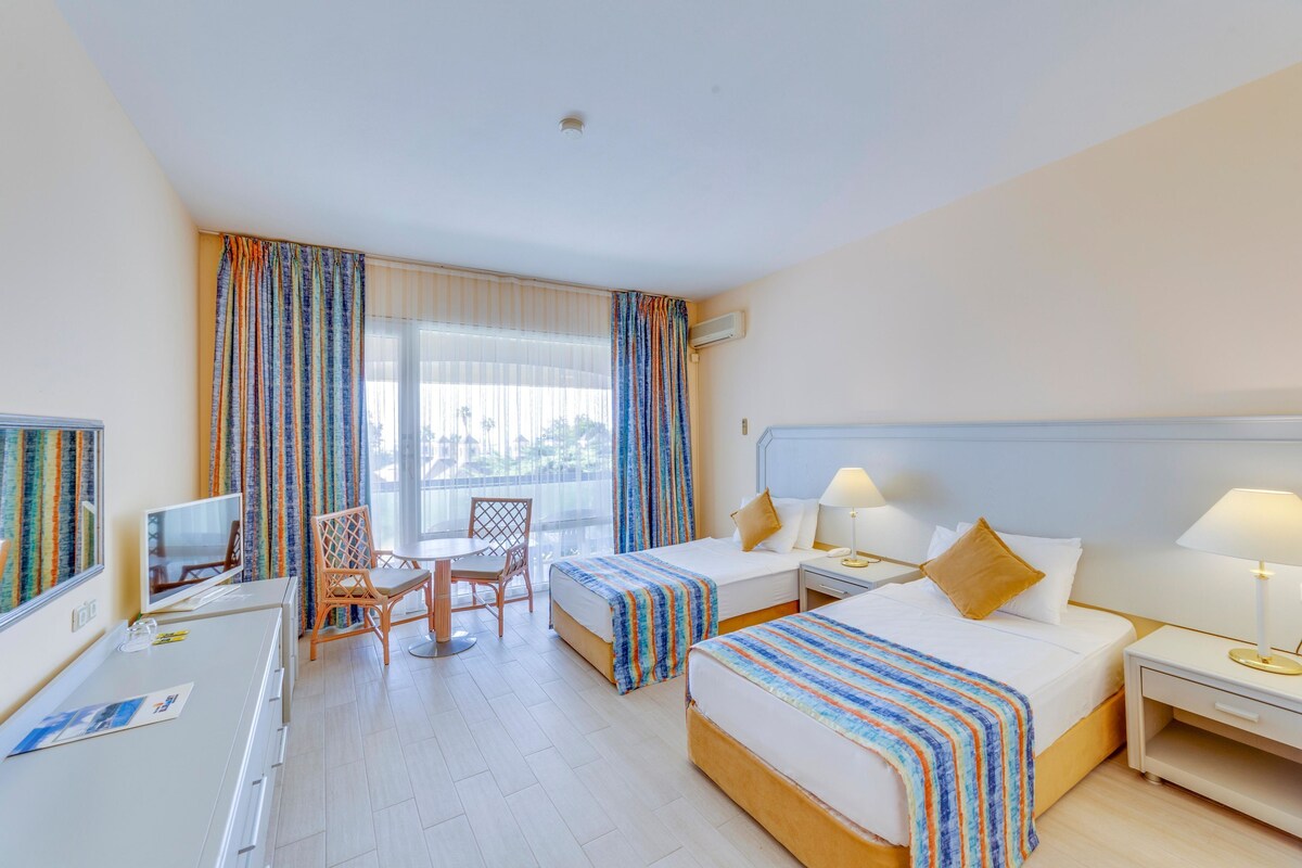 Een hotelkamer met twee bedden, een bureau, een stoel, een televisie en een raam met gordijnen.