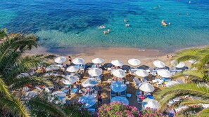 Une plage avec une eau d’un bleu limpide, des chaises longues, des parasols et des palmiers.