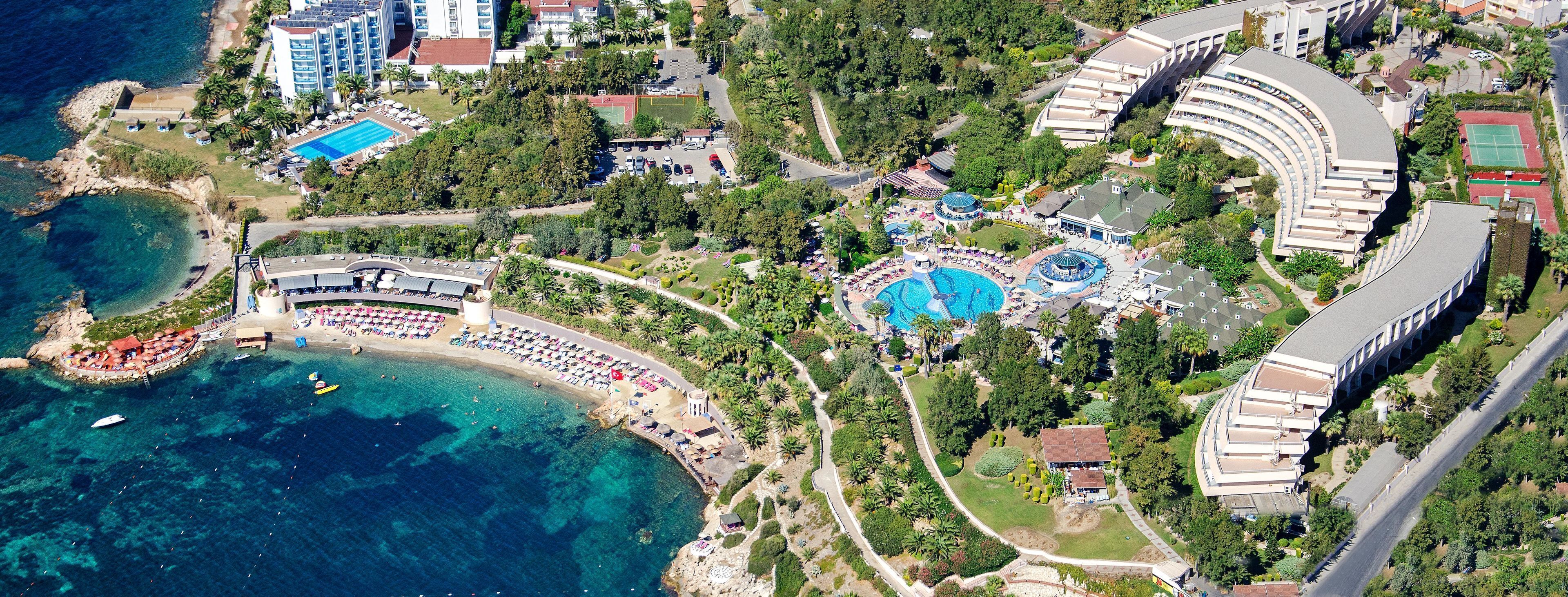 An aerial view of a resort with a large pool, multiple buildings, and a beach area.