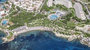 An aerial view of a coastal resort with multiple hotel buildings, a central pool area, and a beachfront promenade. - The Grand Blue Sky International (Kusadasi)
