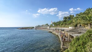 A coastal area with a pier, palm trees, and a building with a lighthouse. - The Grand Blue Sky International (Kusadasi)