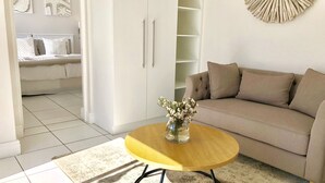 A modern living room with a beige sofa, a round wooden coffee table with a vase of flowers, and a white cabinet with shelves. - 5 Options (Cape Town)