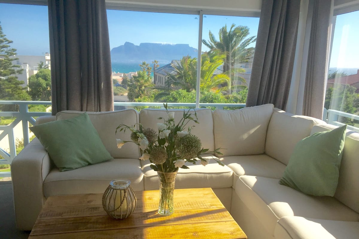 A white sofa with green cushions, a wooden coffee table, and a vase with flowers.