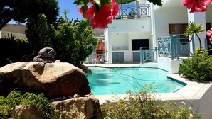 A swimming pool with a stone border, a white building with a balcony, and lush greenery. - 5 Options (Cape Town)