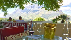 A table with a sandwich, a glass of wine, and a bottle of water, set against a scenic mountain backdrop. - 5 Options (Cape Town)