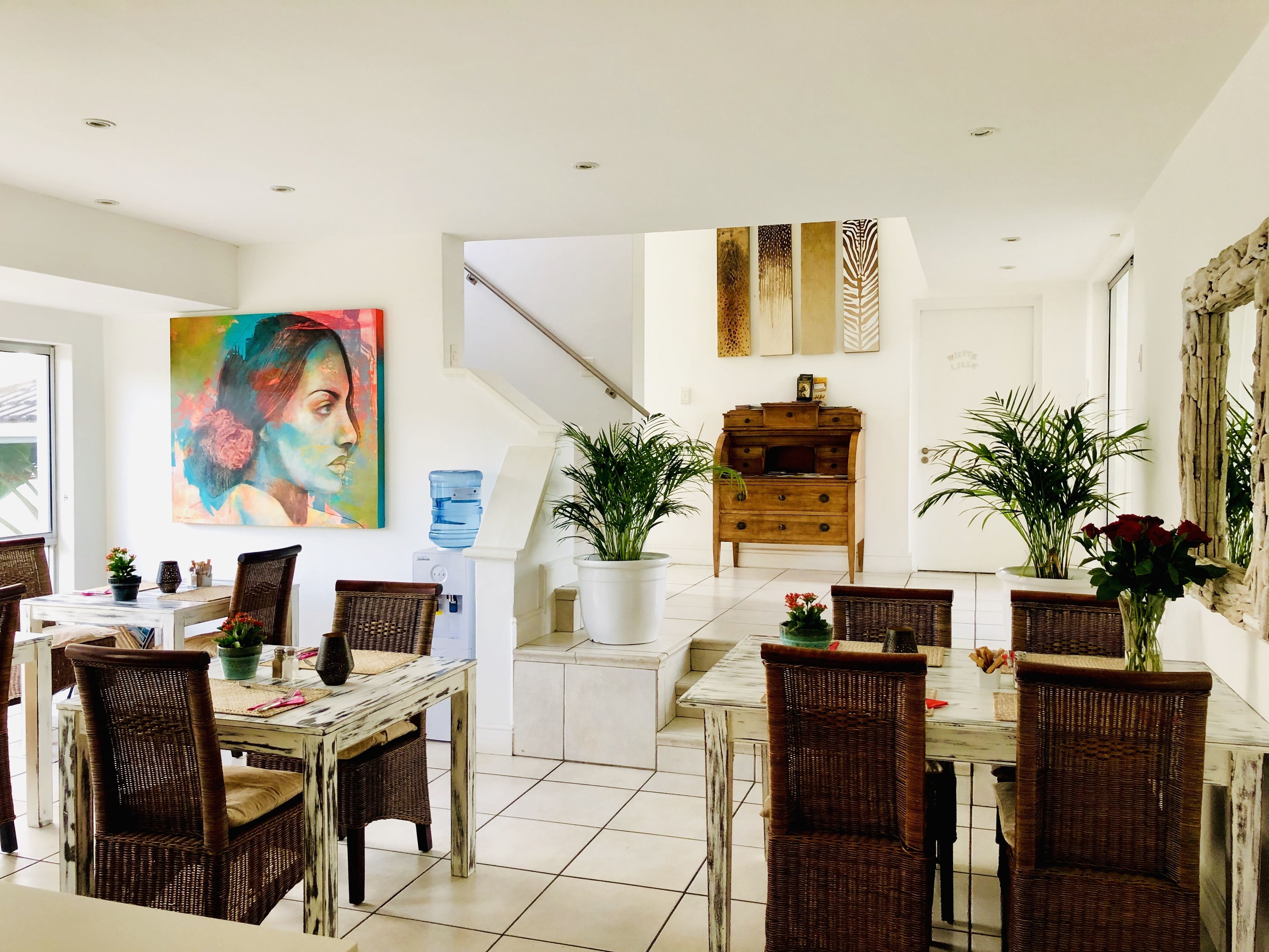 A dining area with a white table, wicker chairs, and a painting on the wall.
