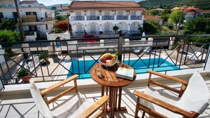 A terrace with a pool, wooden chairs, and a table with a book and fruit. - Studios Diamanto (Kefalonia)