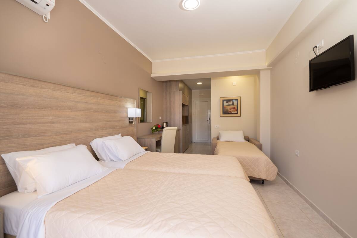 A hotel room with two beds, a desk, a chair, a TV, and a bathroom visible through an open door.