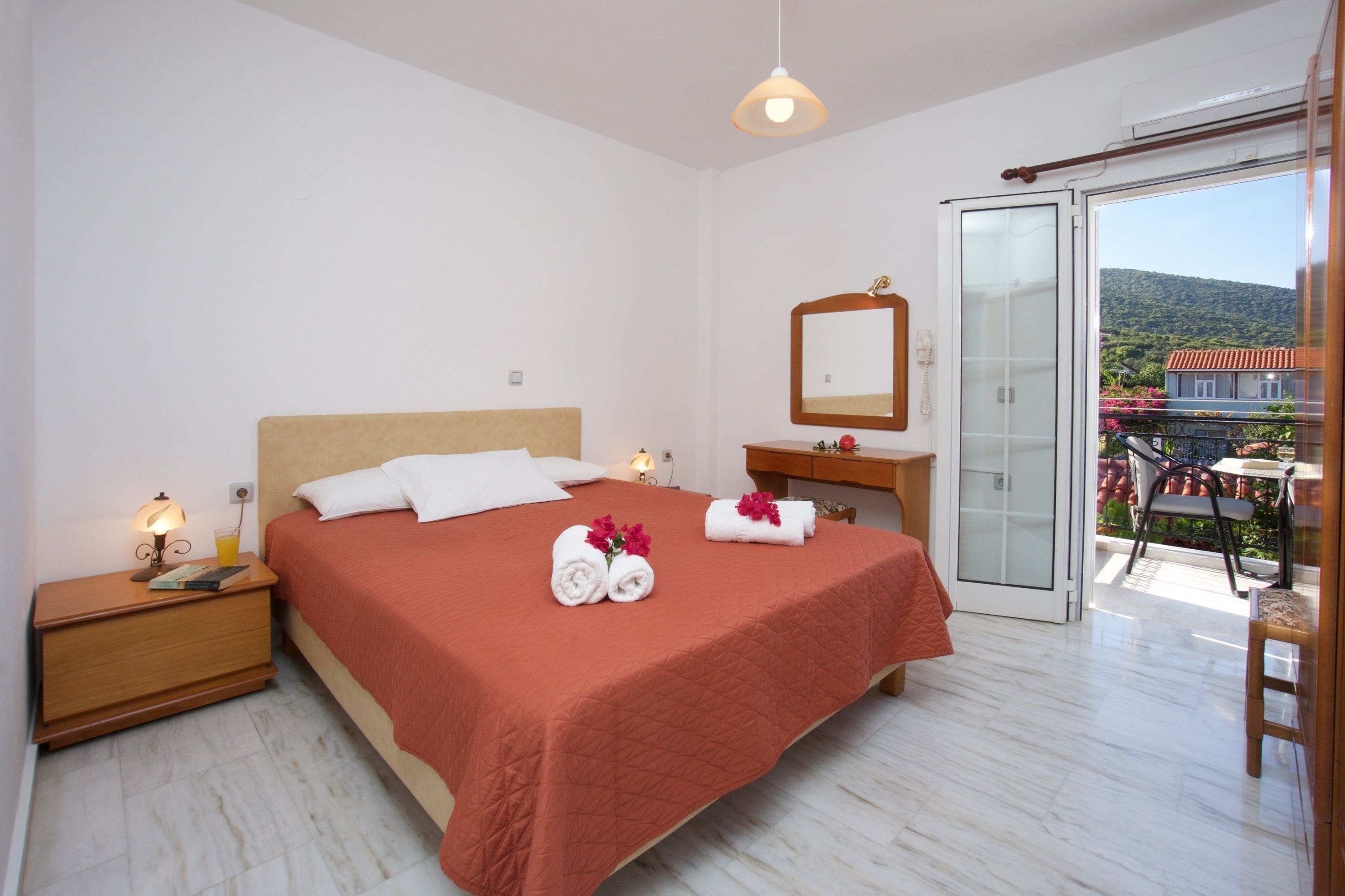 A bedroom with a bed, a nightstand, a dresser, a mirror, and a balcony with a table and chairs.