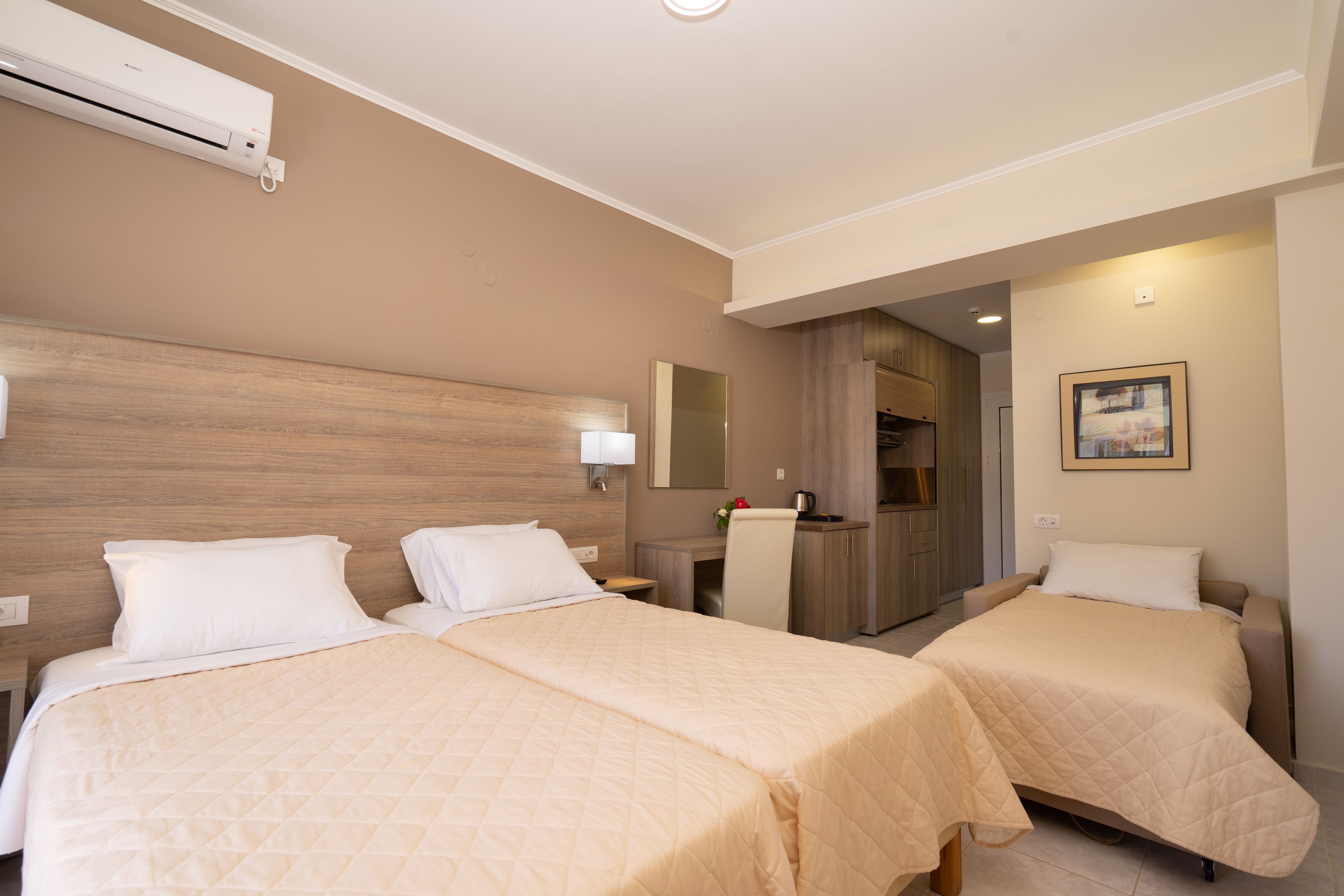 Hotellihuone, jossa on kaksi sänkyä, työpöytä, peili ja ilmastointilaite.