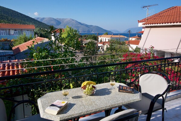 A balcony with a table set for two, a book, and a bowl of fruit.