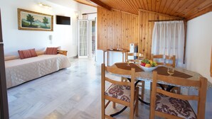 A cozy room with a wooden ceiling, a bed with a quilted cover, a dining table with chairs, and a bowl of fruit. - Studios Diamanto (Kefalonia)