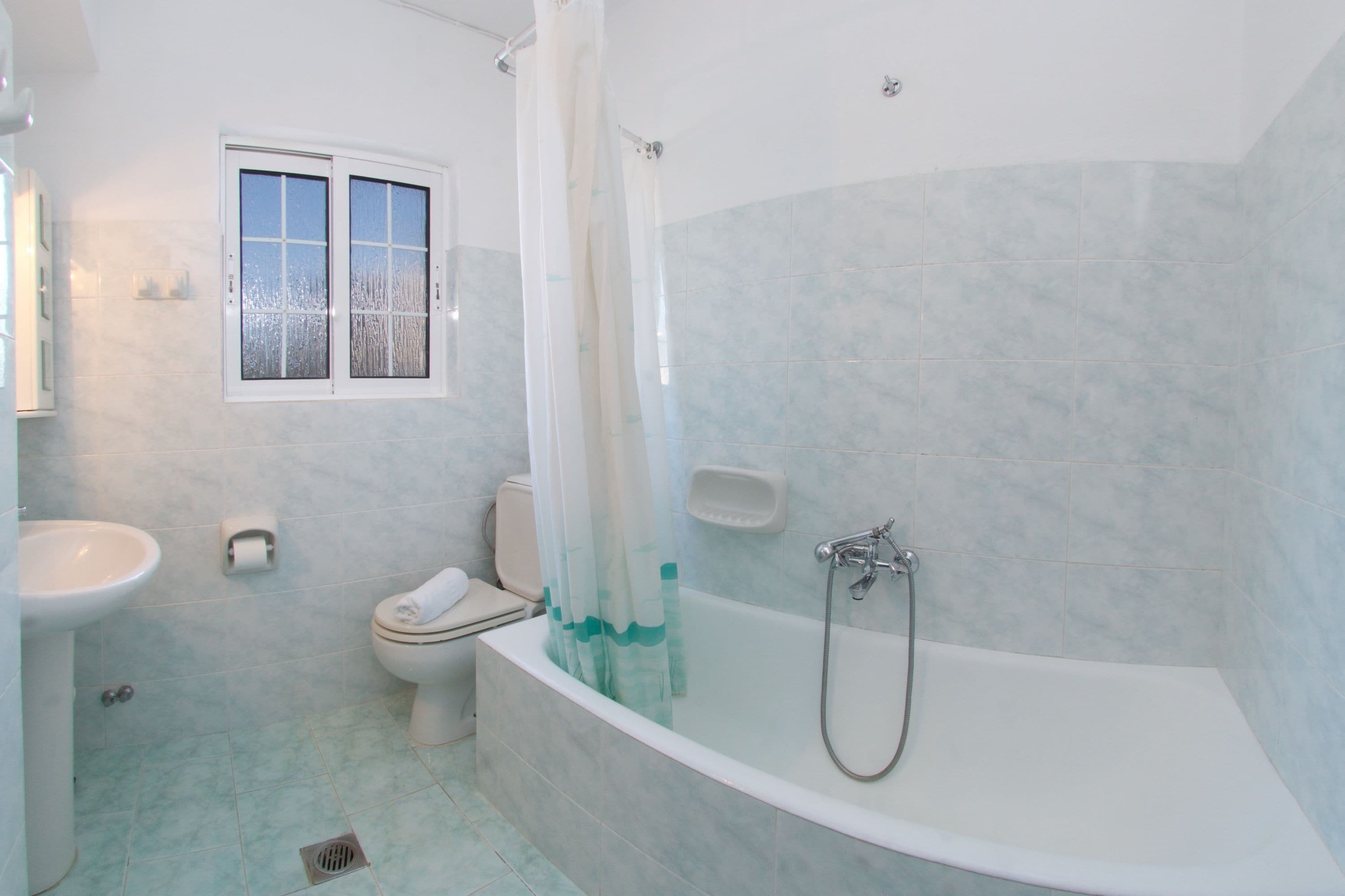 Un baño con bañera, inodoro, lavamanos y ventana.