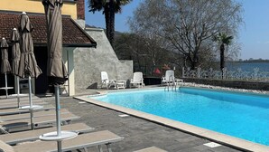 Una piscina con sillones de descanso y sombrillas, un muro de piedra y vista al mar.