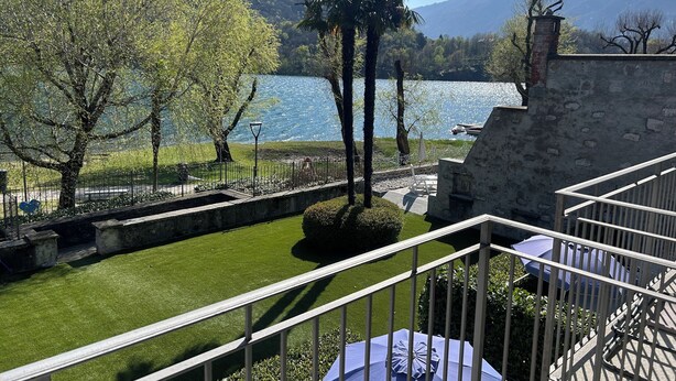 Una terraza con vista a un lago y montañas, muros de piedra y barandilla.