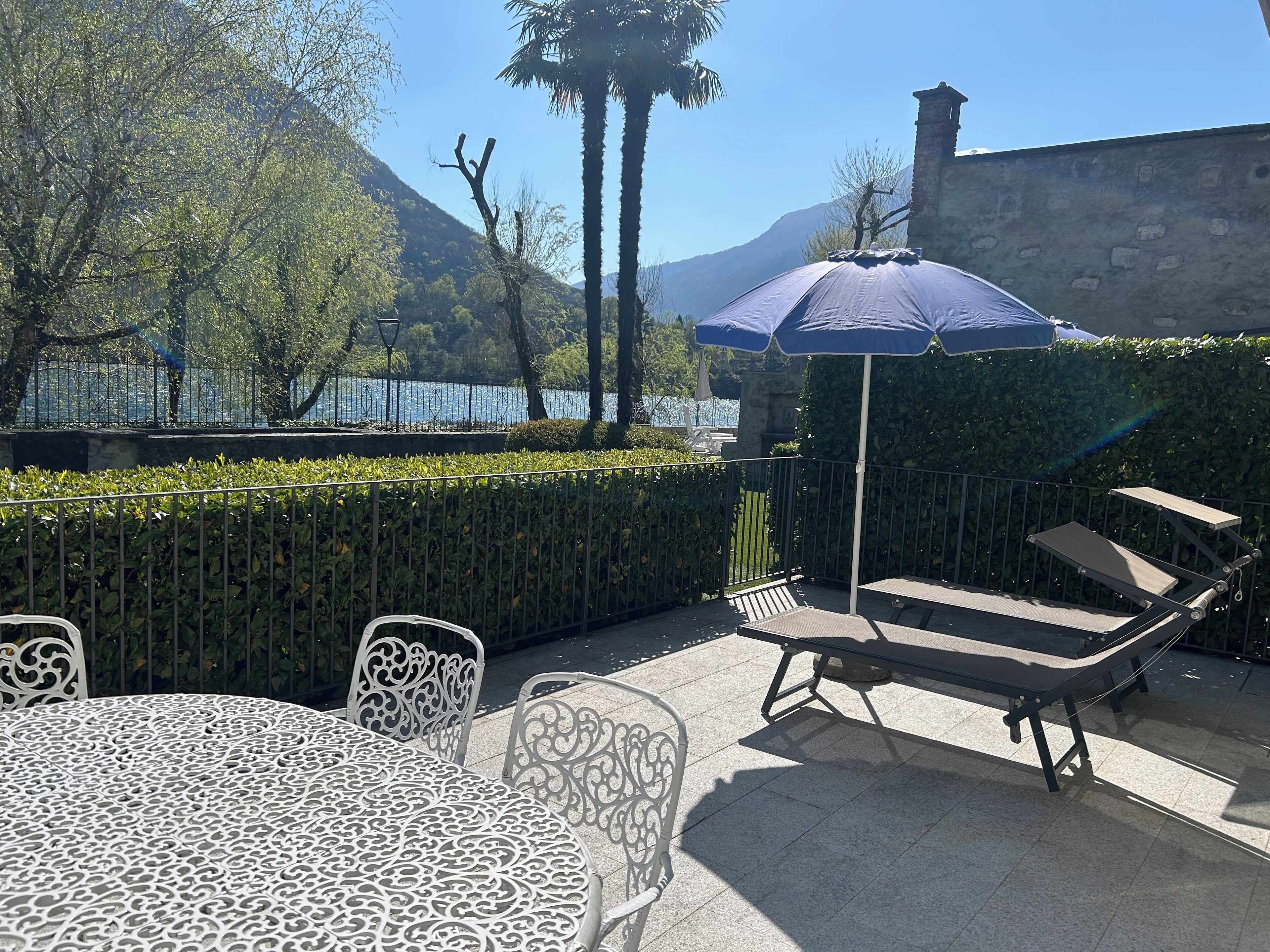 Un patio exterior con mesa y sillas, una silla de lounge y una sombrilla azul.