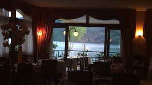 Un restaurante con mesas dispuestas para comer, vistas a un lago y cortinas en las ventanas.