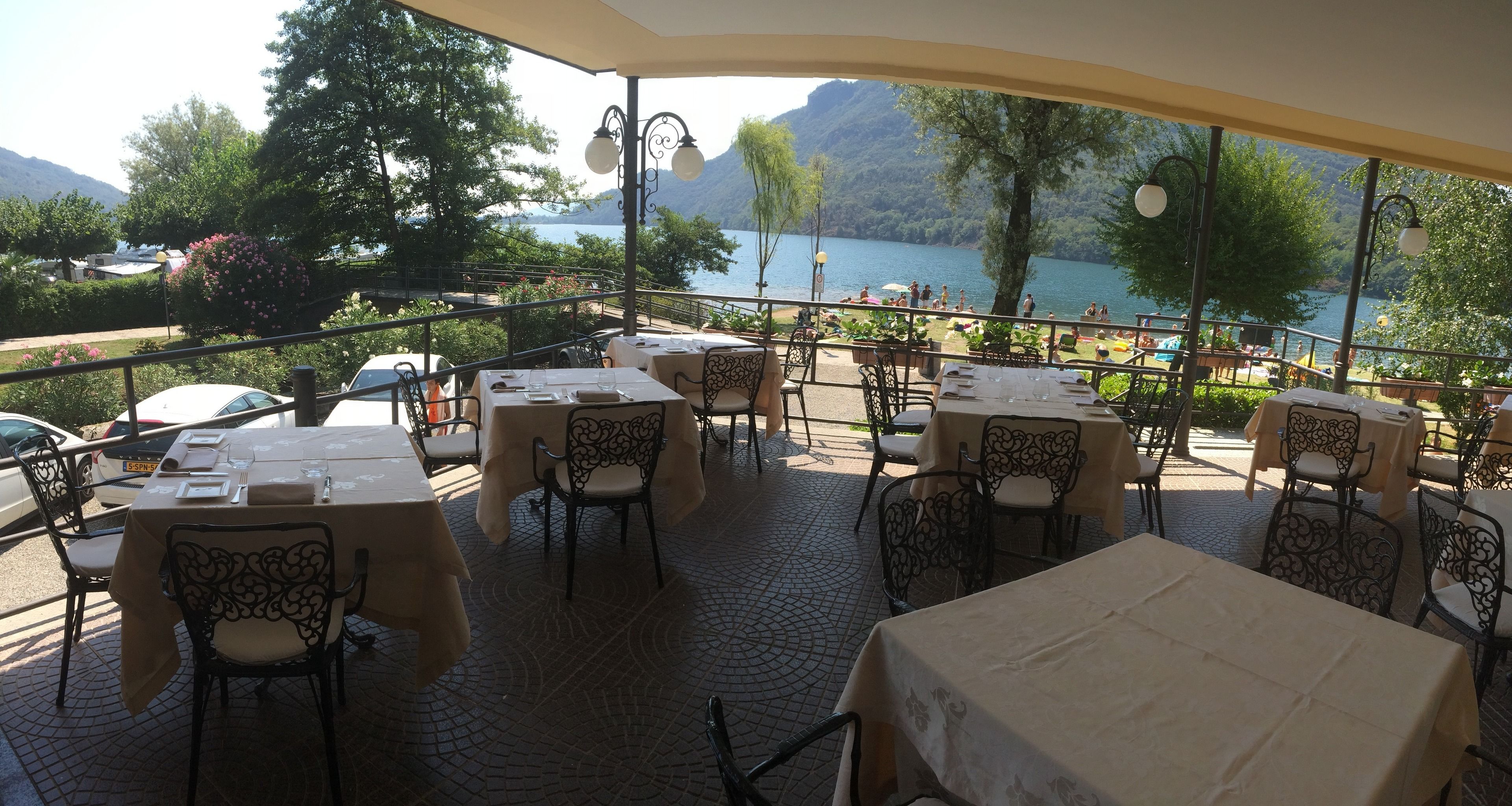 An outdoor terrace with tables and chairs, overlooking a lake and mountains.