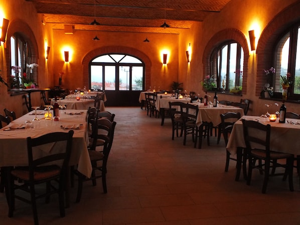 A restaurant with multiple tables set for dining, featuring a warm interior with brick walls and arched windows.