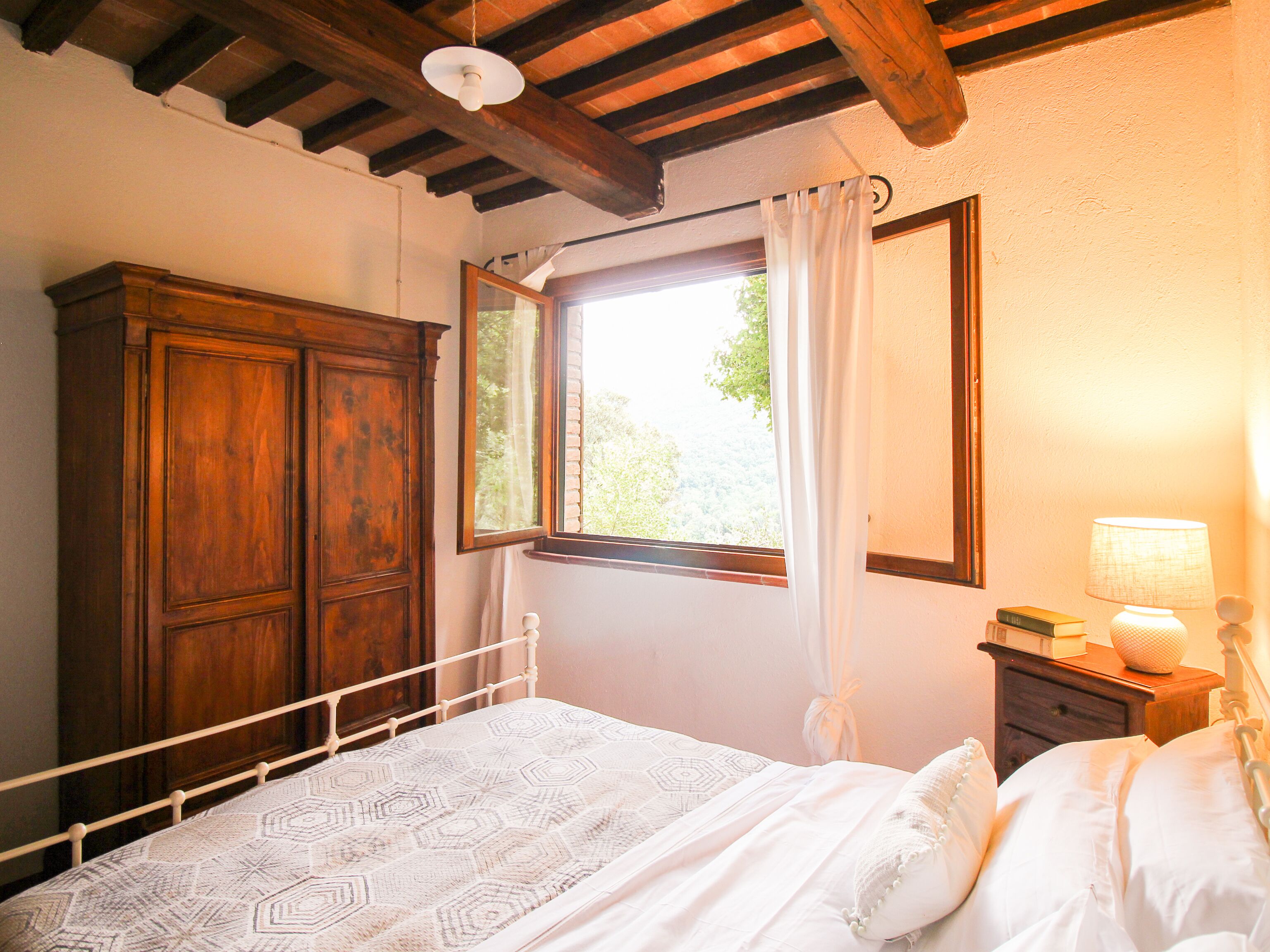 Een slaapkamer met een houten garderobe, een bed met een bedsprei met patroon, een nachtkastje met een lamp en een raam met gordijnen.