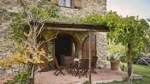 An outdoor patio with a stone wall, wooden furniture, and a pergola covered with climbing plants. - Boschi di Montecalvi (Suvereto)