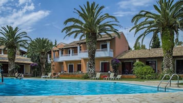 Un área de piscina con una piscina azul cristalina, sillas de descanso y palmeras.